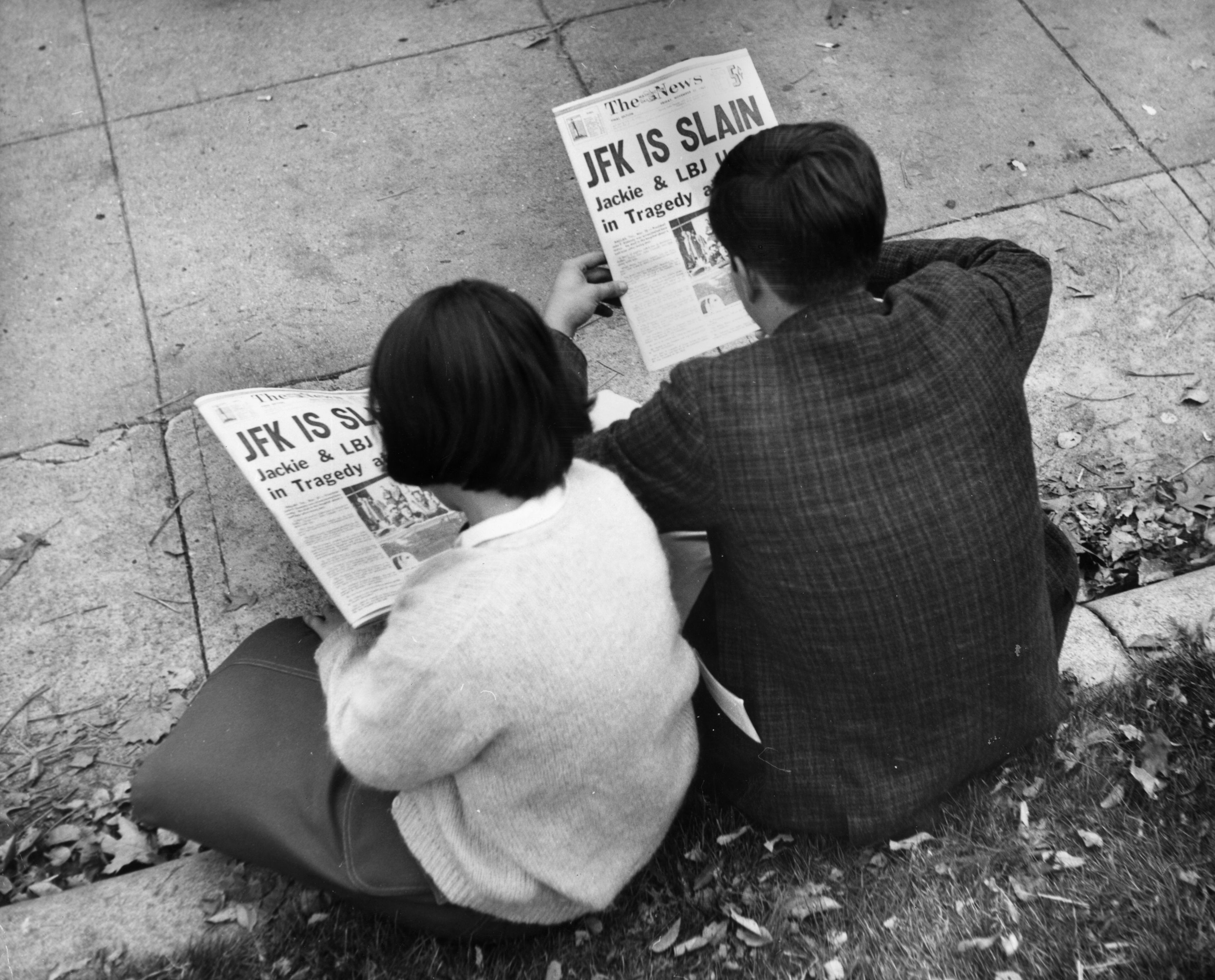 Two people sit in Lafayette Park in Washington, D.C. on Nov. 25, 1963 reading the newspaper reports of President John F. Kennedy's assassination. (credit: Keystone/Getty Images)